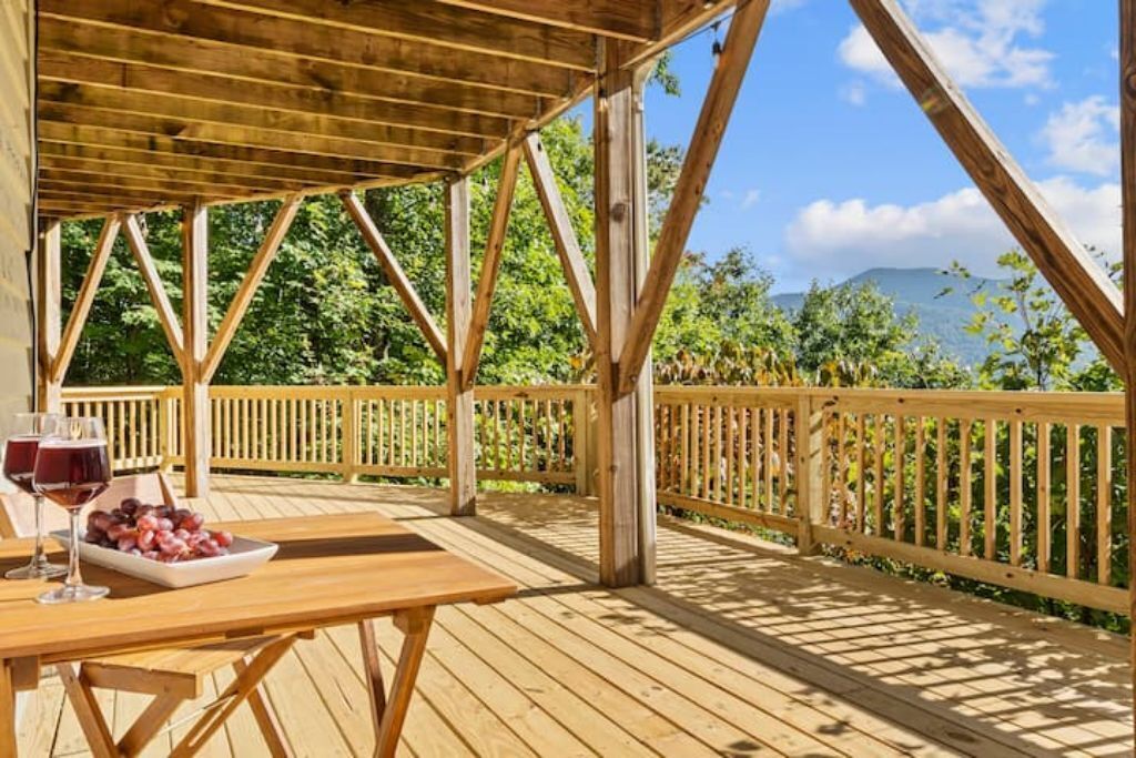 Une terrasse en bois avec une table et des chaises, une balustrade, et une vue sur la verdure et une montagne en arrière-plan.