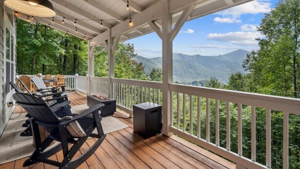 A wooden deck with a white railing, outdoor furniture, and a view of mountains.