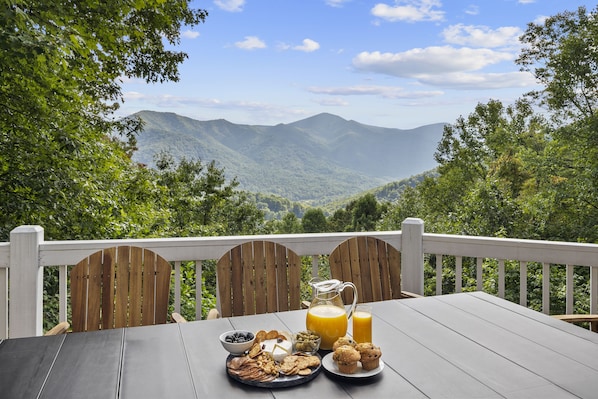 A wooden deck with a table set for breakfast, overlooking a mountainous landscape.