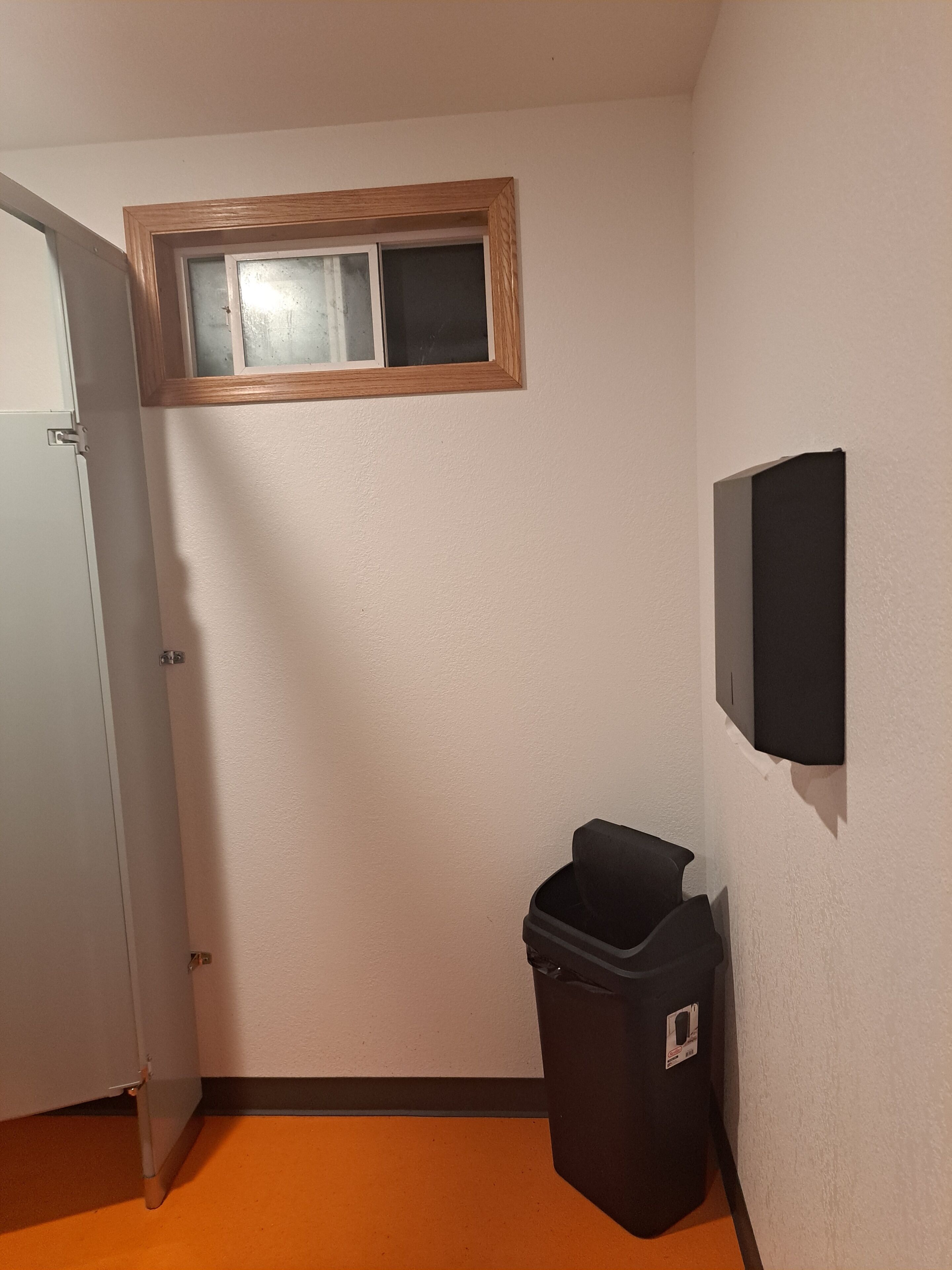 Un couloir avec une porte, une poubelle, une fenêtre et un appareil fixé au mur.