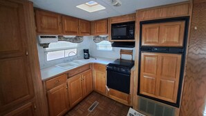 A compact RV kitchen with wooden cabinets, a microwave, a stove, and a refrigerator. - 03 Dutchmen Classic that sleeps 1- 6 people comfortably for the perfect weekend  (Cloquet)