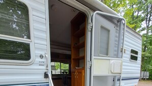 A recreational vehicle with a door open, revealing a storage area with shelves and a step leading inside. - 03 Dutchmen Classic that sleeps 1- 6 people comfortably for the perfect weekend  (Cloquet)