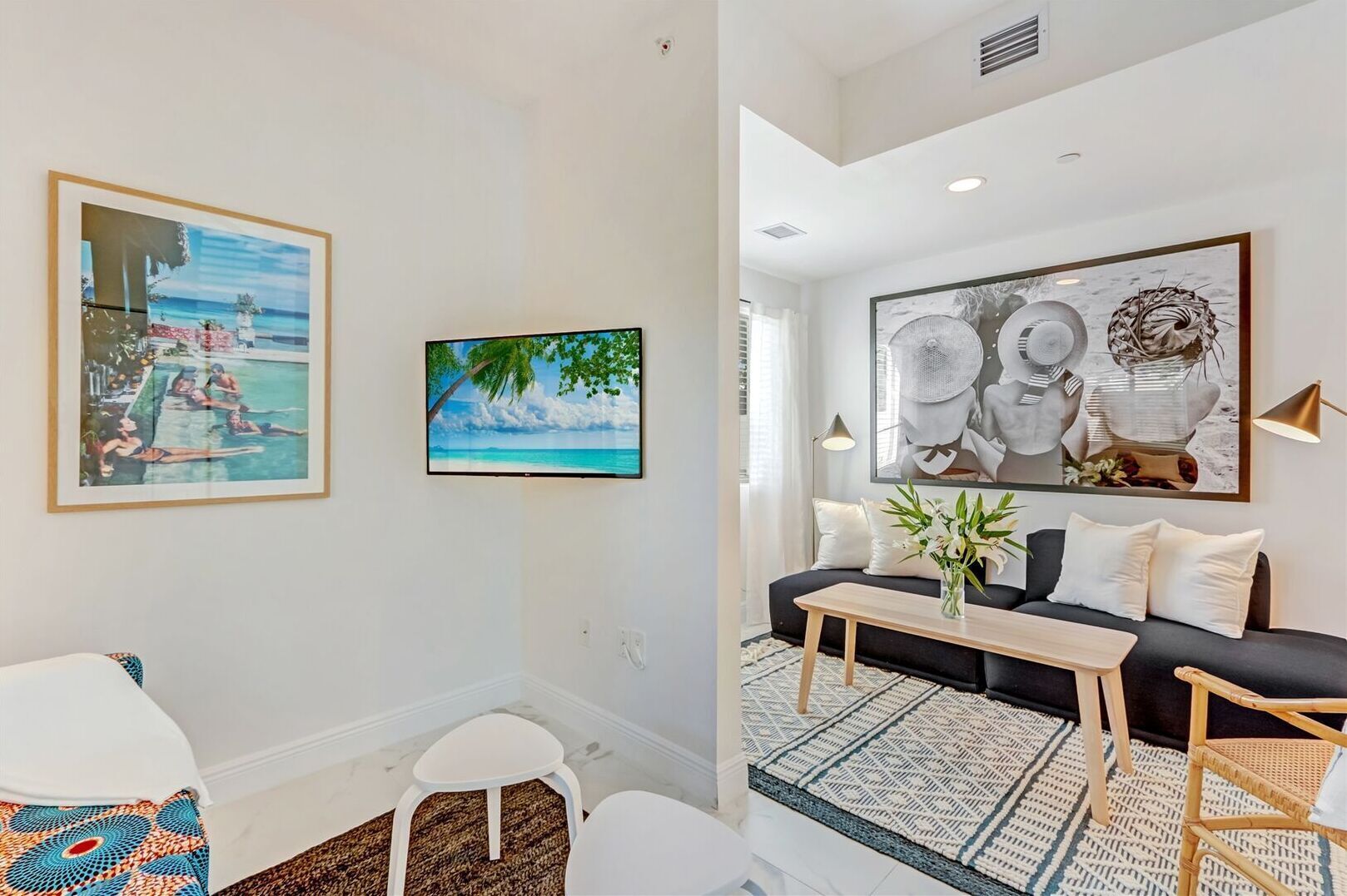 A modern living room with a black sofa, a coffee table, and a large abstract painting. There are two framed pictures on the wall, a small white table, and a patterned rug.