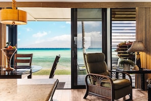 Una habitación con vista al océano, una silla de mimbre, una mesa con una lámpara y una planta en una mesita auxiliar.