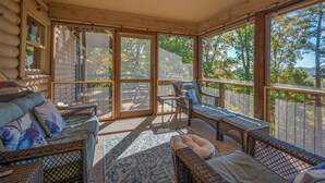 Una cabaña de troncos con un porche cubierto, que incluye muebles de mimbre y ventanas amplias.