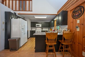 A compact kitchen with dark cabinets, a white refrigerator, a microwave, and a wooden island with two chairs.