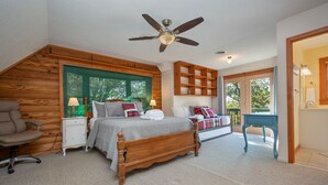 Un dormitorio con cama de madera, un escritorio, una silla, ventilador de techo y vistas al exterior.