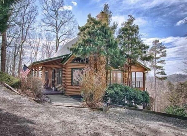 Une cabane en rondins avec un porche, entourée d’arbres et sous un ciel dégagé.