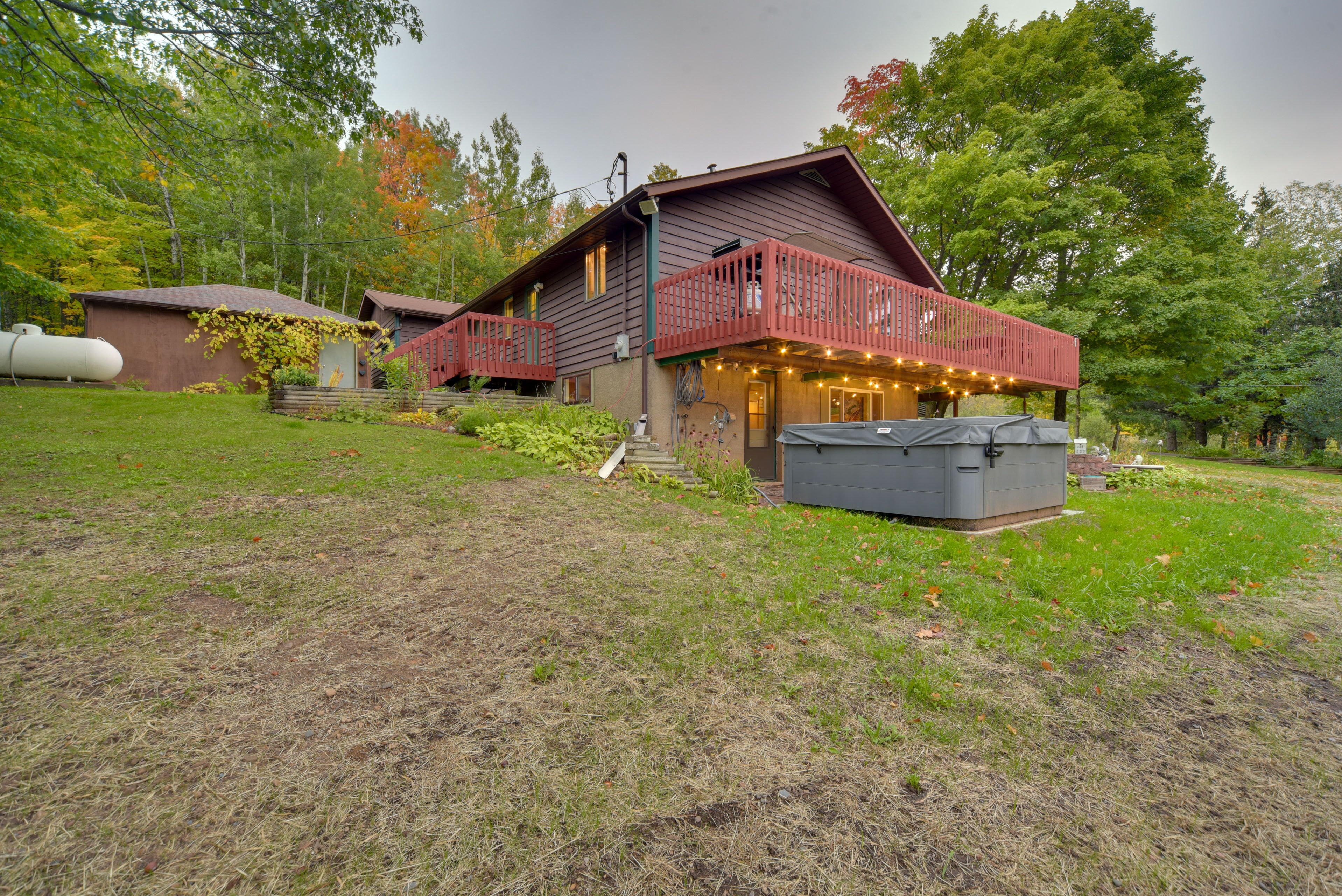 Un chalet rustique avec un balcon rouge, un espace salon extérieur abrité et un grand réservoir d’eau en arrière-plan.