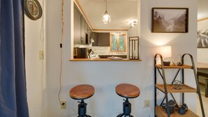Una cucina con un grande specchio, sgabelli di legno, una lampada a sospensione e uno scaffale con utensili da cucina.