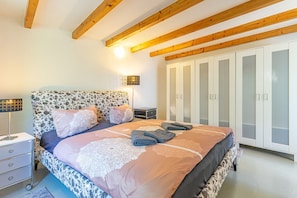 Un dormitorio con cabecera de flores, una cama con cubrecolcha de encaje, una mesita de noche con lámpara y un armario con puertas espejadas.
