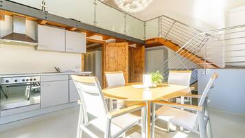 A modern kitchen with a built-in oven, a dining table with chairs, and a staircase with a glass railing.