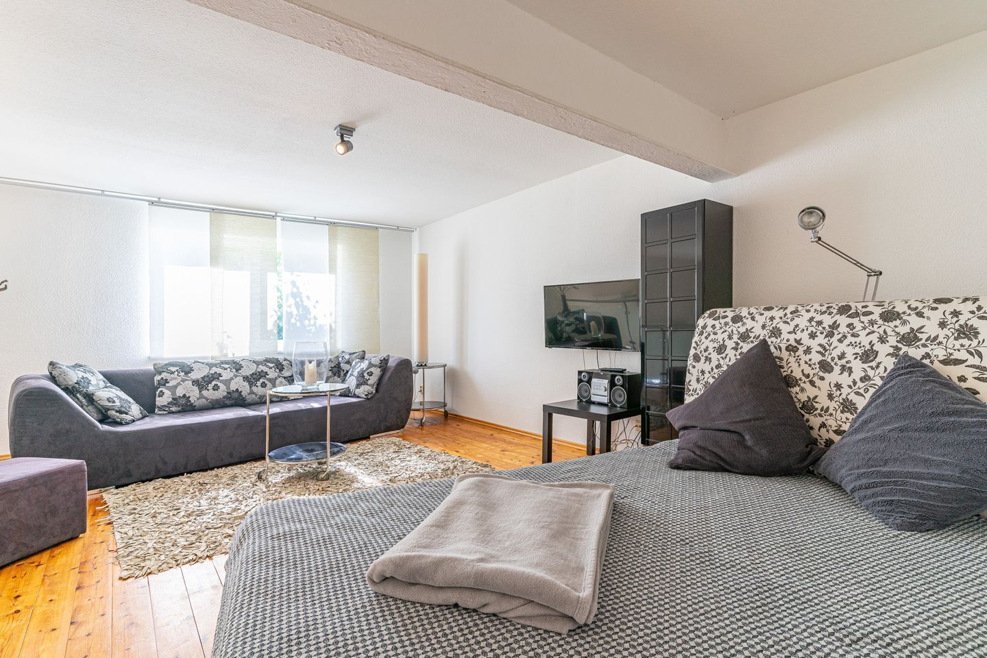 A modern living room with a grey sofa, a patterned armchair, a coffee table, and a flat-screen TV mounted on the wall.