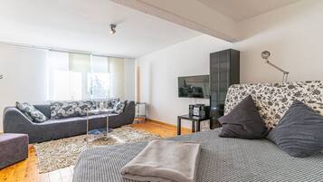 A modern living room with a grey sofa, a patterned armchair, a coffee table, and a flat-screen TV mounted on the wall.