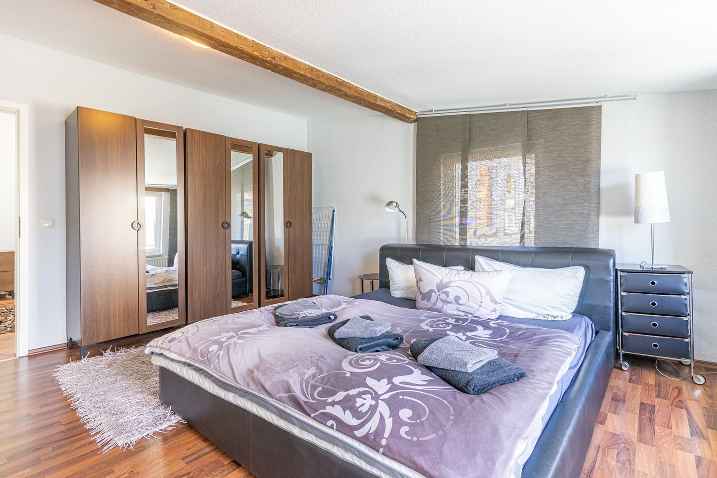 A bedroom with a large bed, a wardrobe, a bedside table, and a mirror.
