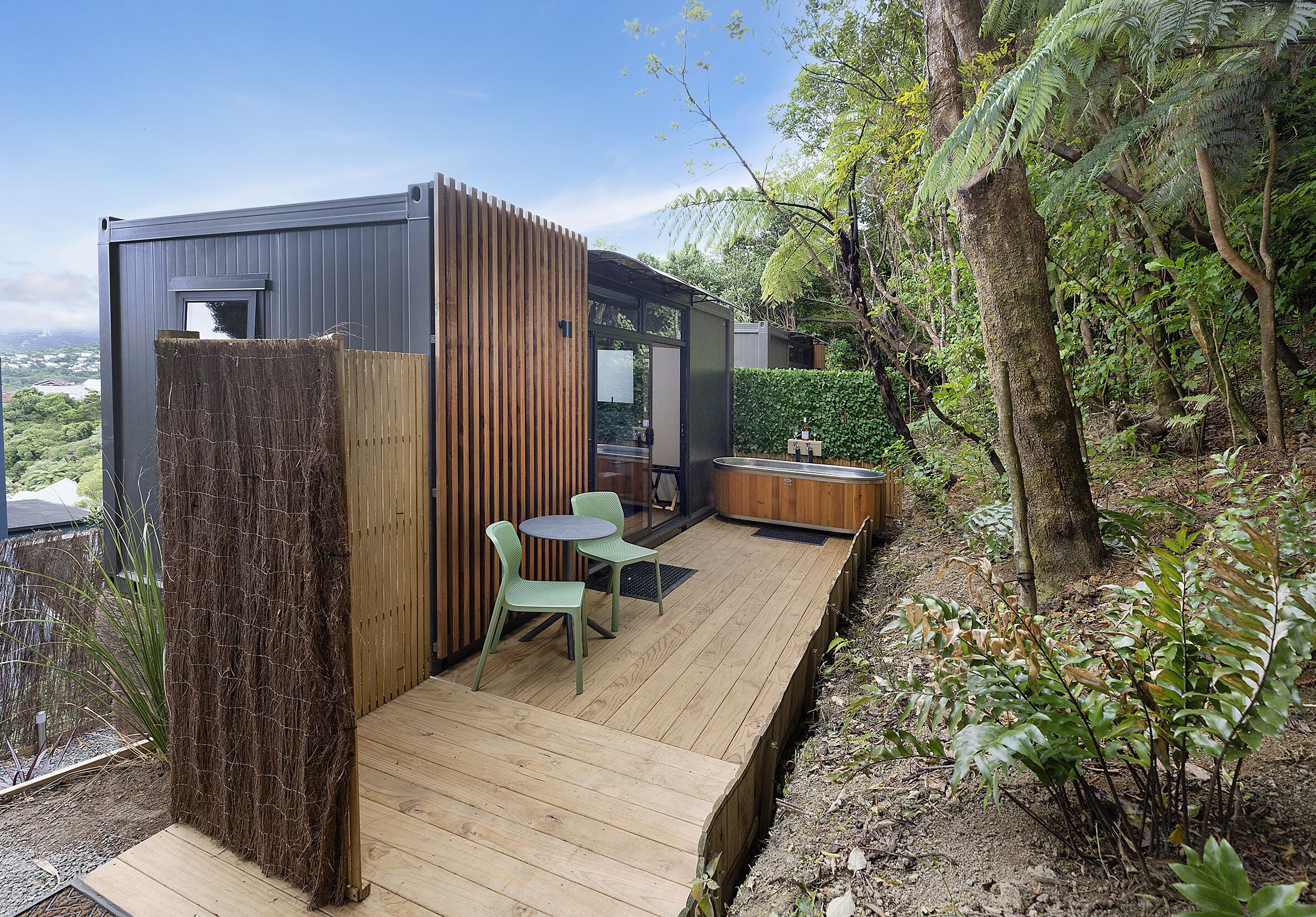 A modern outdoor deck with a wooden table and chairs, surrounded by lush greenery and a view of the landscape.