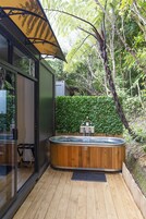 Una terraza de madera con un jacuzzi, rodeada por una cerca de madera y abundante follaje.