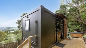 Un bâtiment moderne et compact, doté d’une grande fenêtre, d’une terrasse en bois et d’un jacuzzi.