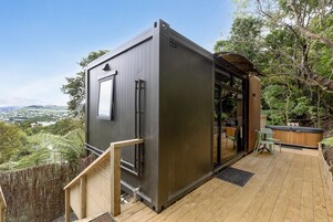 Un edificio moderno y compacto con un ventanal grande, una terraza de madera y un jacuzzi.