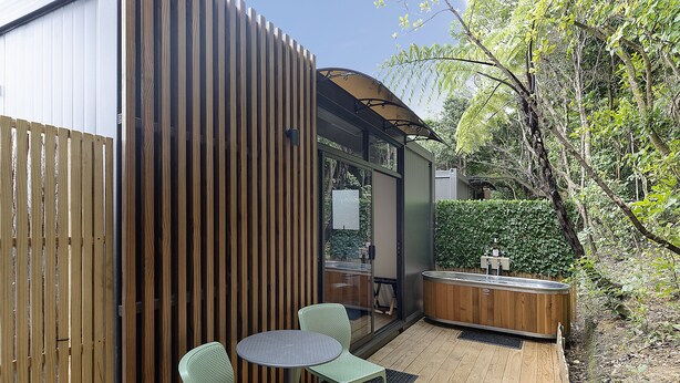 Une terrasse en bois avec une table ronde et deux chaises, un jacuzzi et une clôture en bois.