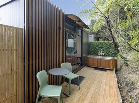 Una terraza de madera con una mesa redonda y dos sillas, un jacuzzi y una valla de madera.