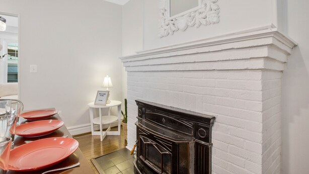A dining area with a white brick fireplace, a white table with a lamp, and red plates on the table.