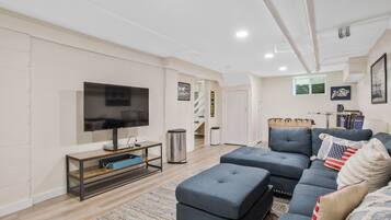 Un salon moderne avec un canapé d’angle, un téléviseur à écran plat et un escalier menant à un autre niveau.