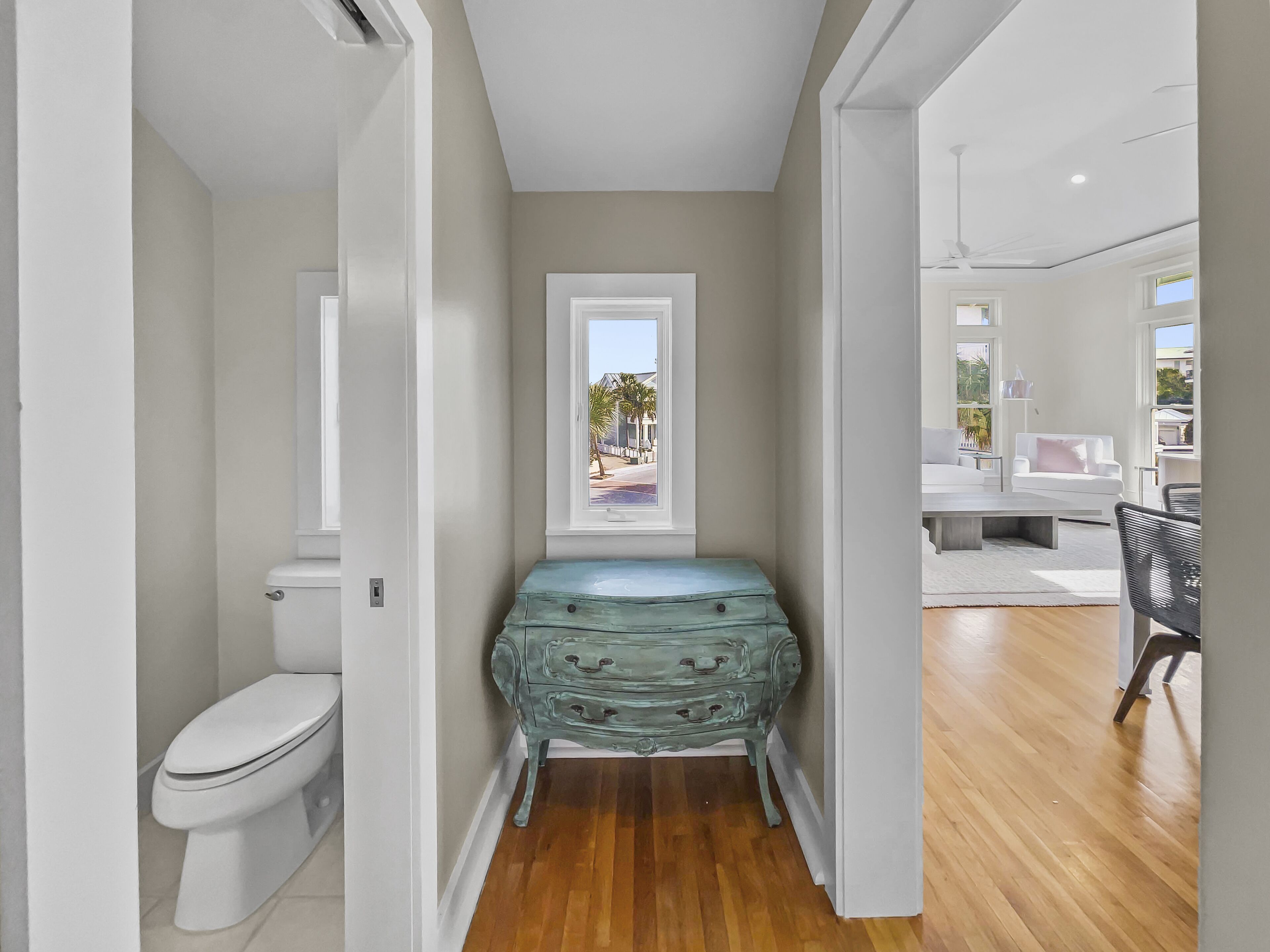 Un baño moderno con inodoro, ventana con vistas a la calle y suelo de madera.