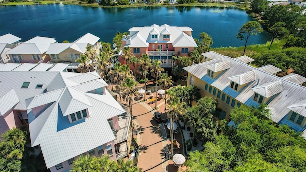 A residential area with houses featuring gabled roofs, a central courtyard with palm trees, and a lake in the background.