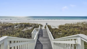 A wooden boardwalk leading to a beach with a clear sky.