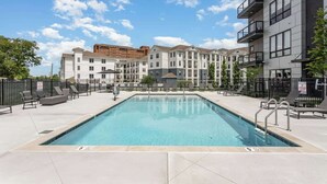 Una piscina con sillones de descanso y un edificio de varios pisos con balcones.