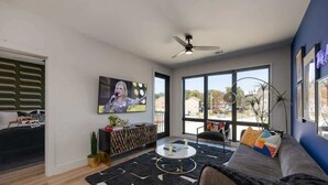Una sala de estar moderna con un sofá, una mesa de centro, televisor y ventanas amplias.