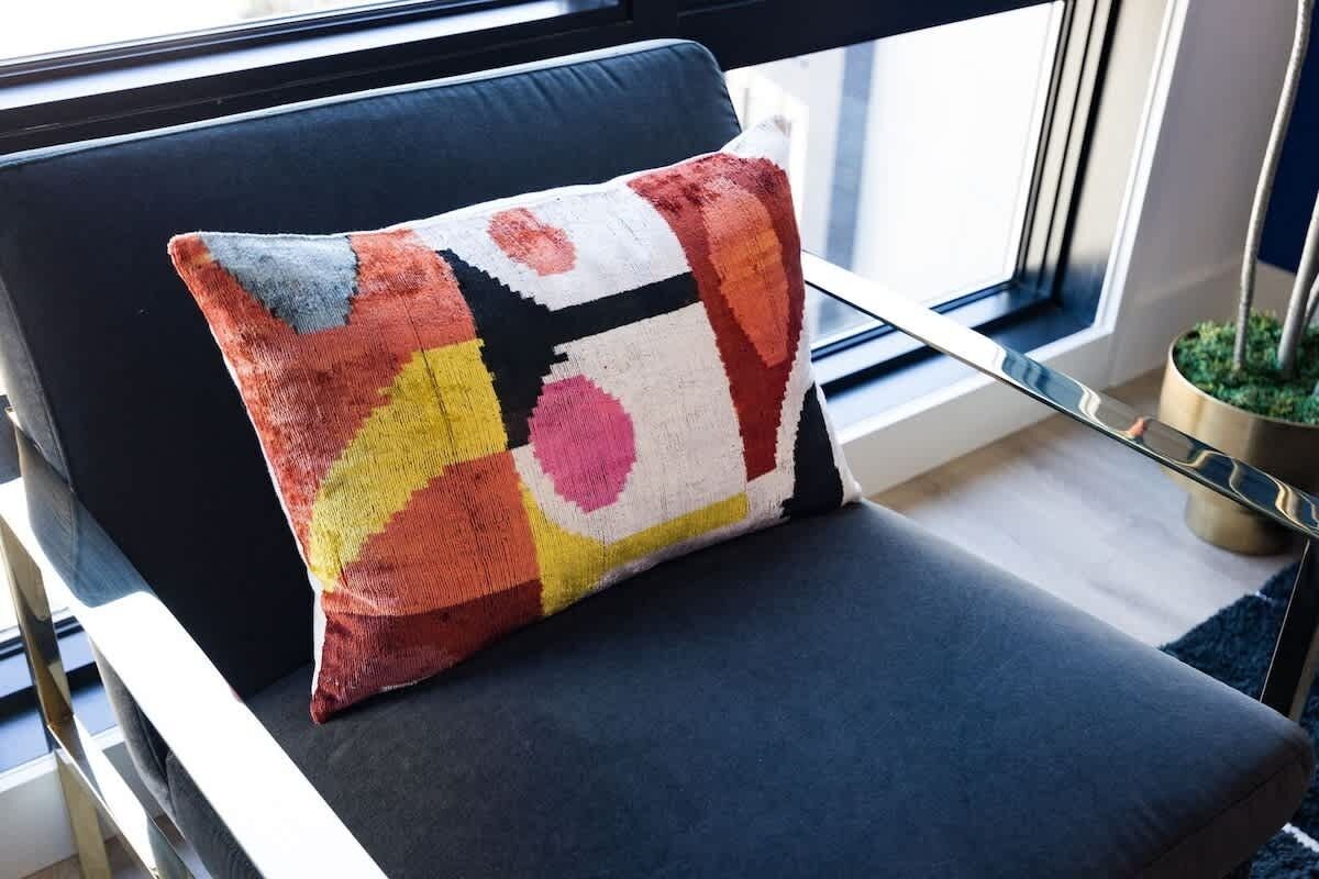 Une chaise avec un coussin coloré, une fenêtre avec des stores et une plante en pot.