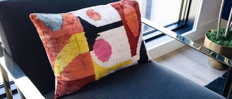 Une chaise avec un coussin coloré, une fenêtre avec des stores et une plante en pot.