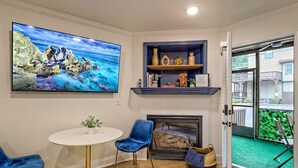 Ein Wohnzimmer mit großem Fernseher, Kamin, rundem Tisch und blauen Sesseln.