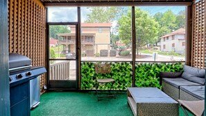 Ein Zimmer mit grünem Teppich, einem Grill, einer Couch und Blick auf Häuser durch große Fenster.