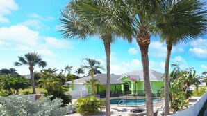 A pool area with palm trees, a green house, and a clear sky. - Pool Paradise with hot tub, bikes, every beach need, games and more! (Cocoa Beach)