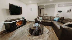 Ein modernes Wohnzimmer mit Fernseher, Kamin, braunem Ledersofa und rundem Couchtisch.