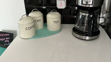 A kitchen counter with a coffee maker, two containers labeled 'COFFEE' and 'TEA', and a welcome sign.