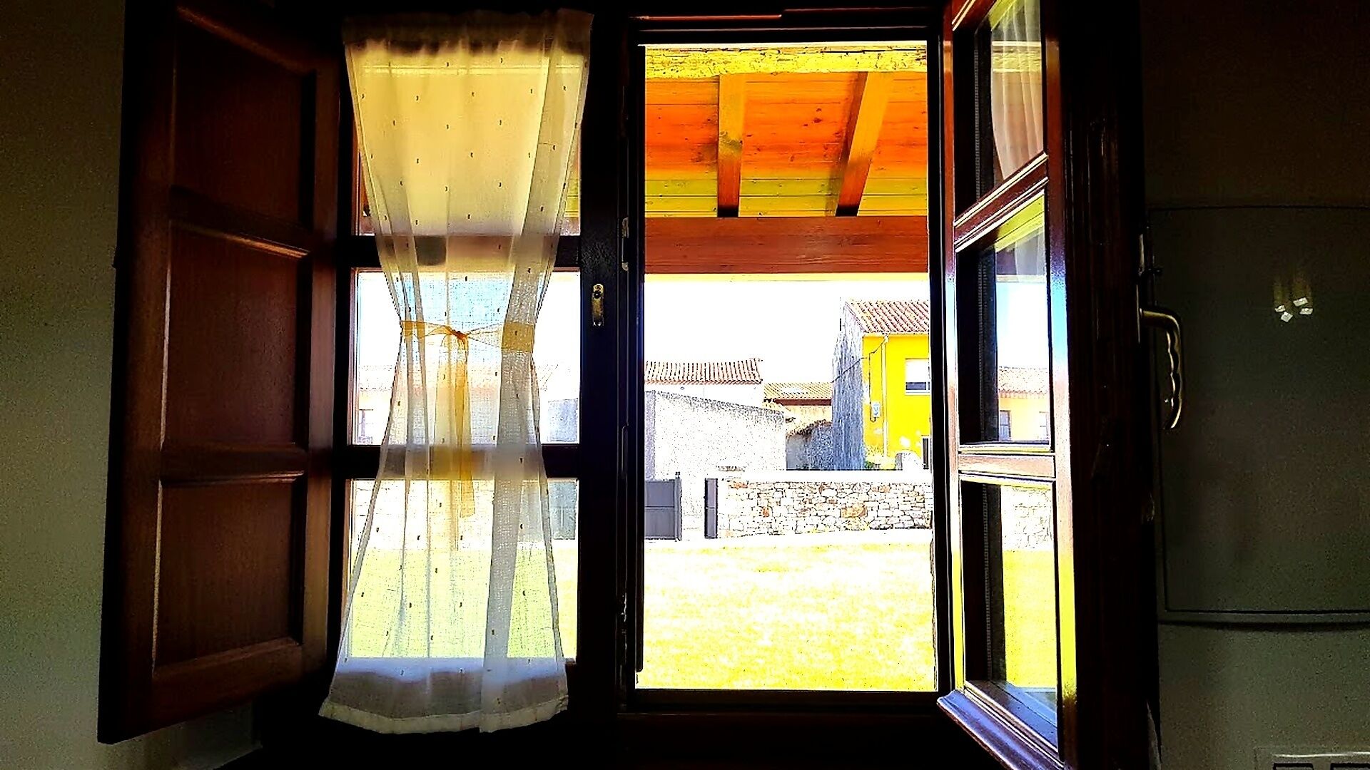 Un vano con marco de madera y una ventana con cortinas traslúcidas.