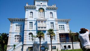 A large, light blue colonial-style building with multiple balconies and a central clock tower. - El Jardín de Casa Male (Pimiango)