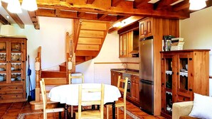 A rustic kitchen with wooden cabinets, a built-in stove, and a dining area with a table and chairs. - El Jardín de Casa Male (Pimiango)