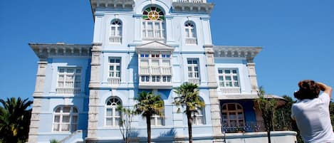 A large, light blue colonial-style building with multiple balconies and a central clock tower.