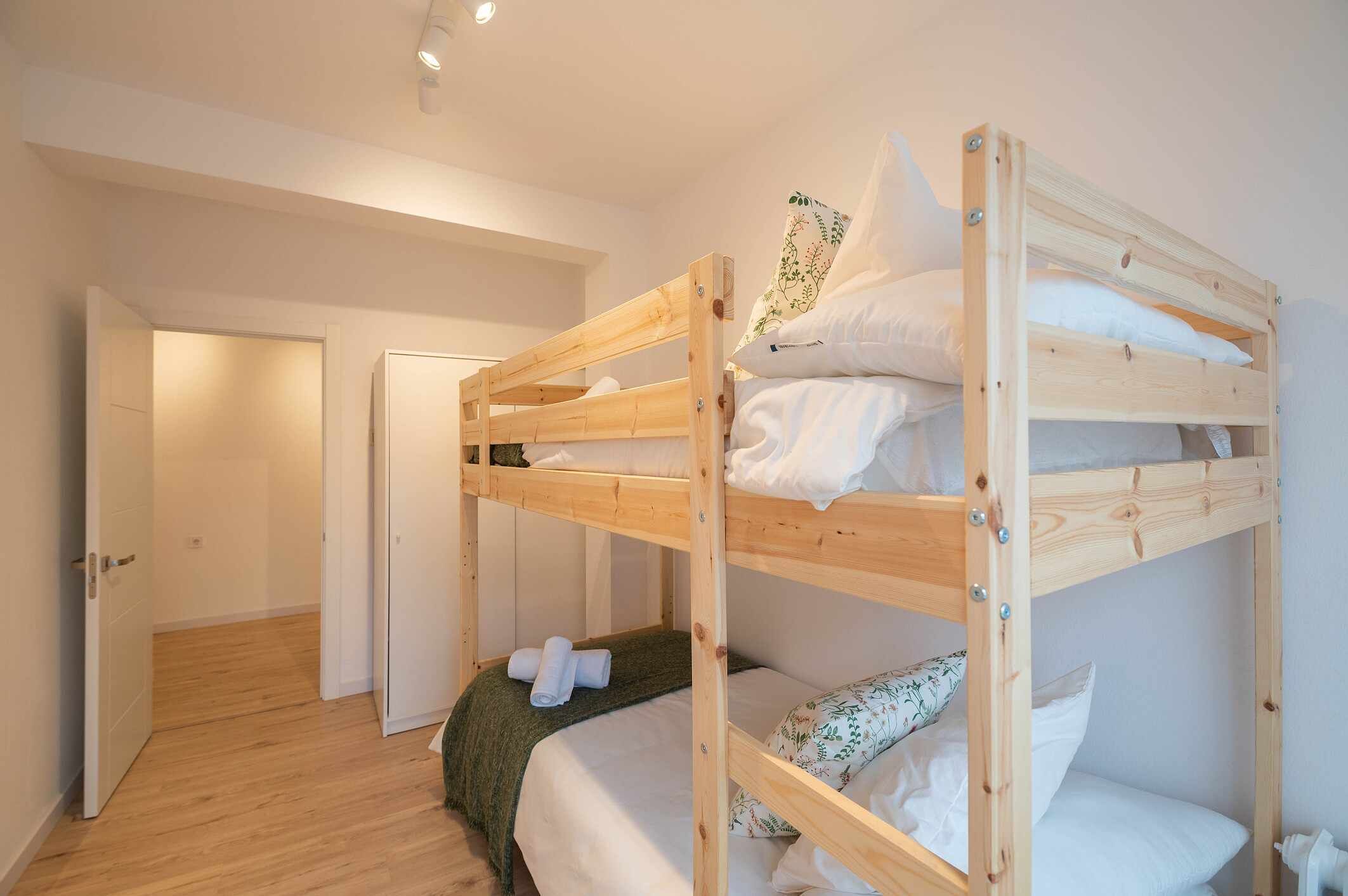Une chambre avec un lit superposé en bois, du linge de lit blanc et une couverture verte.