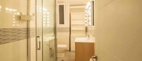 A modern bathroom with a glass shower enclosure, a toilet, and a vanity with a mirror and lights.