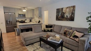 A modern living room with a sectional sofa, a coffee table, and a dining area with a kitchen in the background.