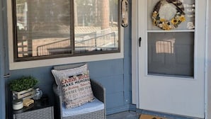 A porch with a wicker chair, a doormat, and a wreath on the door.