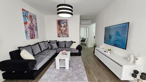 Ein modernes Wohnzimmer mit einem Ecksofa, einem weißen Couchtisch und einem Fernseher auf einem weißen Schrank.
