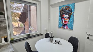 Ein Essbereich mit einem runden Tisch, zwei Stühlen, einem Bild an der Wand und einem Fenster mit Blick nach draußen.