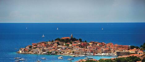 A coastal town with a dense cluster of buildings, a prominent church, and a clear view of the sea with several sailboats.